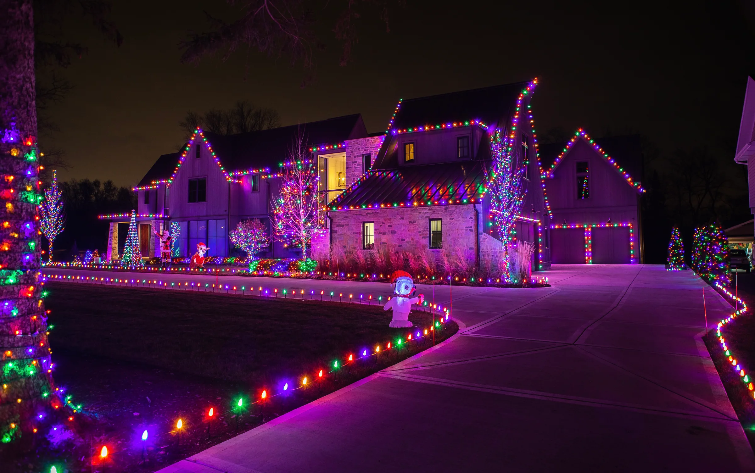 Grand home with red and white roofline lights and illuminated landscaping