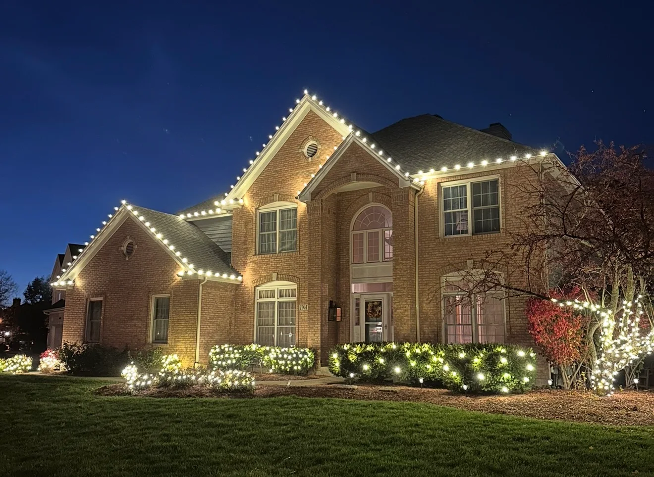 Large brick home with a crisp warm-white roofline and glowing landscape shrubs