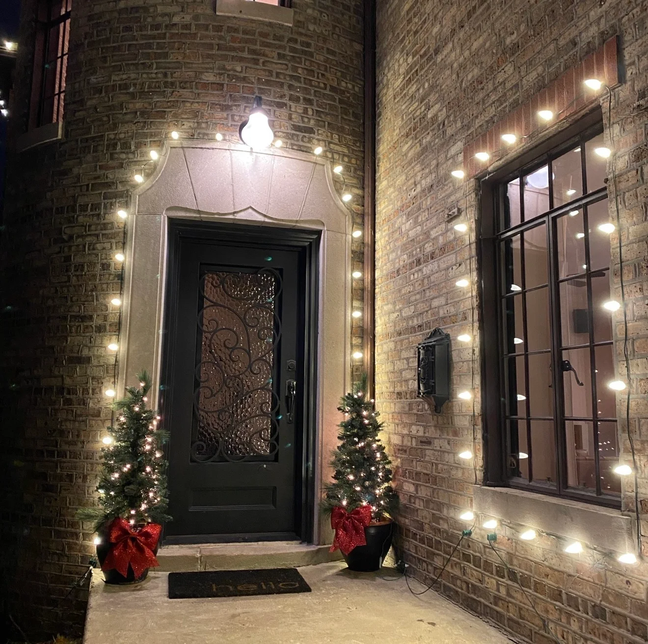 Brick entry framed with warm-white lights and decorated porch trees