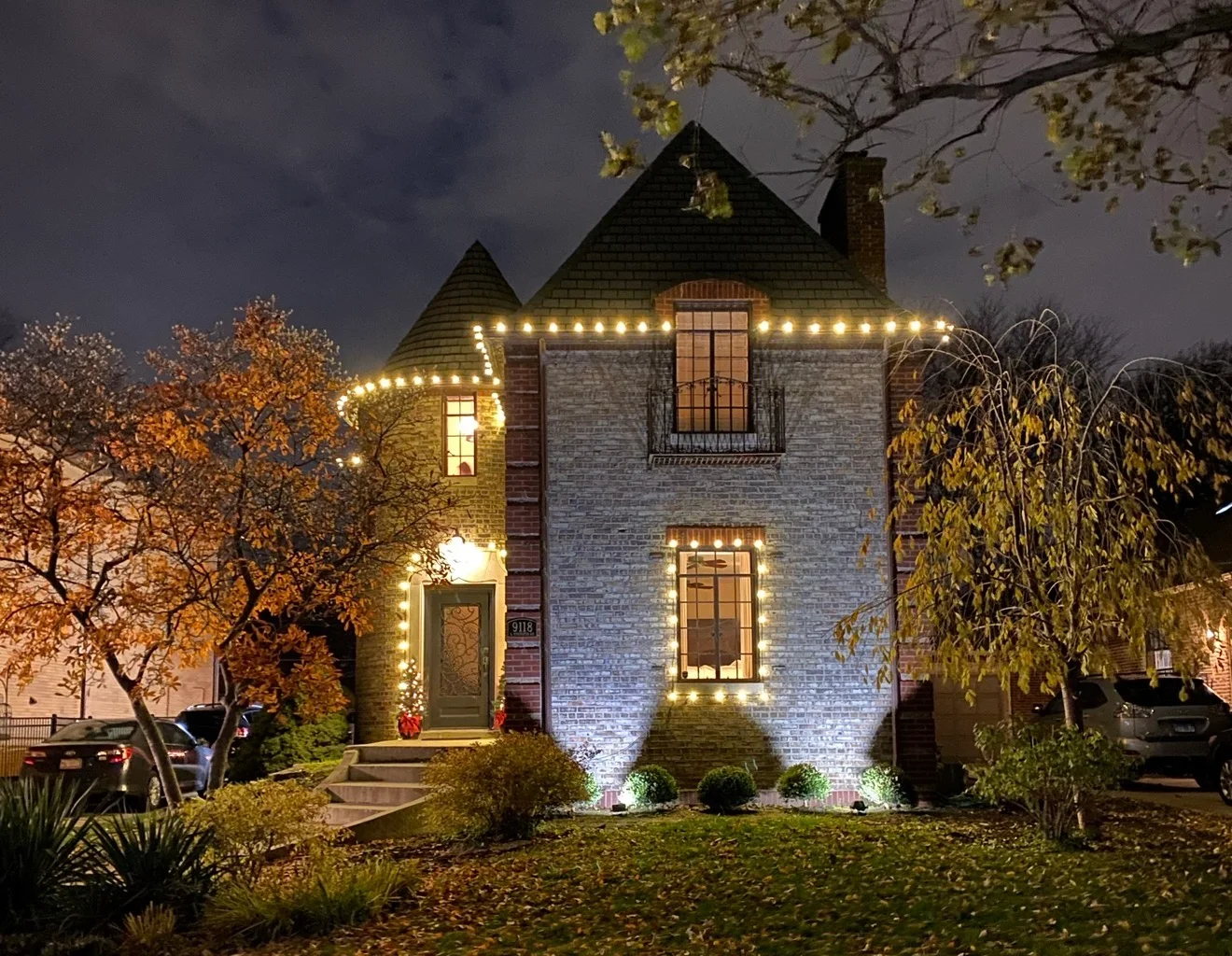Two-story brick home glowing with warm-white roofline, window, and entry lighting