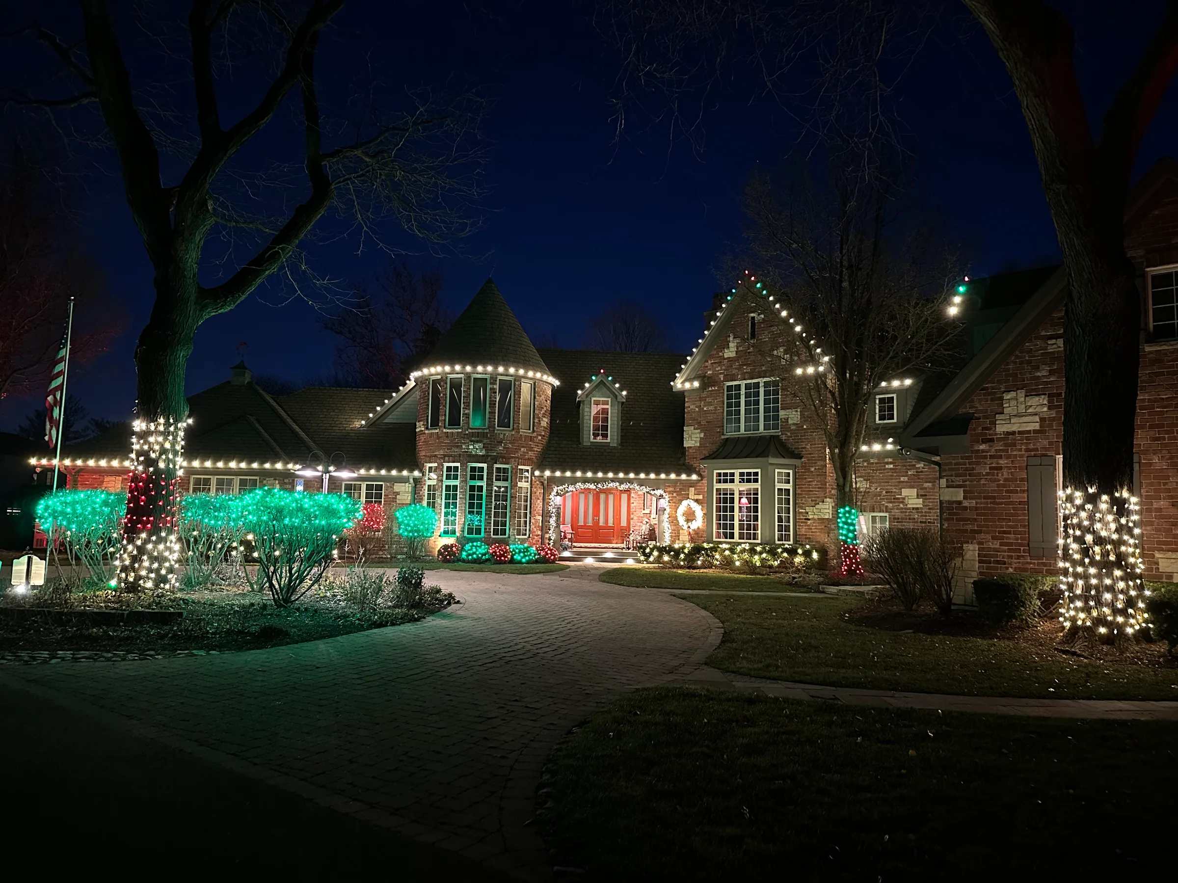 Warm white rooflines with red and green landscape lighting on a large brick home